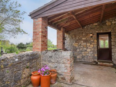 A covered stone patio with brick pillars and three terracotta pots with flowers at Canny Croft in Chilton Polden near Street