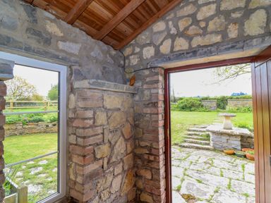 An interior corner with stone walls a window and an open door leading to a stone patio and garden at Canny Croft in Chilton Polden near Street