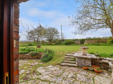 A garden with stone steps leading to a lawn with trees and a stone birdbath at Canny Croft in Chilton Polden near Street