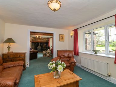 A living room with brown leather sofas wooden coffee table and a window with red curtains at Canny Croft in Chilton Polden near Street