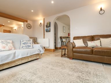 A living room with two sofas a small wooden table and a wall clock at Woodbine Cottage in Mylor Bridge Nr Falmouth