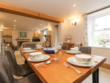 A dining room with a wooden table set for six people and a living room with sofas and a fireplace at Woodbine Cottage in Mylor Bridge Nr Falmouth