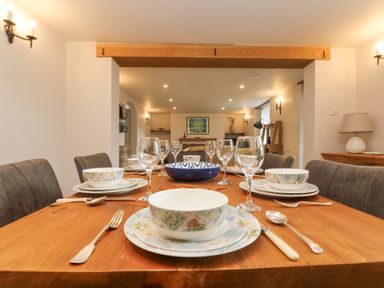 A dining room with a wooden table set with bowls plates cutlery and glasses at Woodbine Cottage in Mylor Bridge Nr Falmouth
