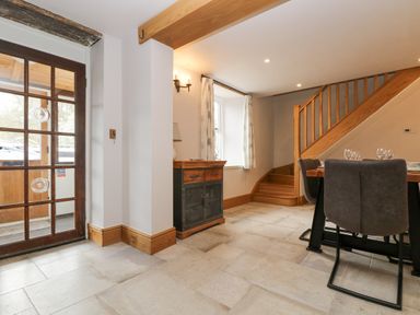 An entrance area with a wooden door next to a small cabinet and stairs leading up beside a dining table with chairs at Woodbine Cottage in Mylor Bridge Nr Falmouth