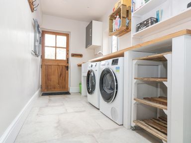 A laundry room with washing machines a wooden door and shelves at Woodbine Cottage in Mylor Bridge Nr Falmouth