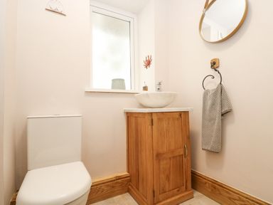 A bathroom with a white toilet a wooden cabinet with a white vessel sink a round mirror and a towel on a ring at Woodbine Cottage in Mylor Bridge Nr Falmouth