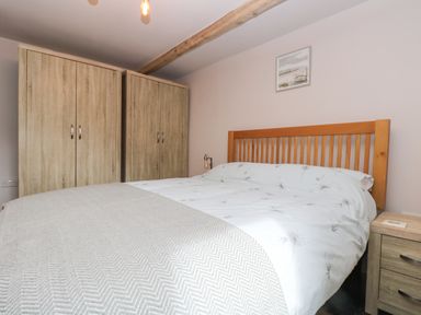 A bedroom with a wooden bed frame two wardrobes bedside table and a wall picture at Woodbine Cottage Mylor Bridge Nr Falmouth