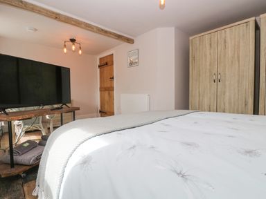 A bedroom with a bed covered with a duvet and blanket a TV on a wooden stand a wooden door and two wardrobes at Woodbine Cottage in Mylor Bridge Nr Falmouth