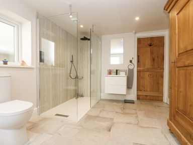 A bathroom with a toilet shower area with glass panels wooden door wooden cabinet and wall-mounted sink at Woodbine Cottage in Mylor Bridge Nr Falmouth