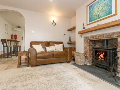 A living room with a brown leather sofa next to a fireplace with a lit wood stove at Woodbine Cottage in Mylor Bridge Nr Falmouth