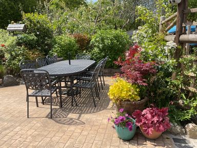 A patio with a black metal table and chairs surrounded by plants and flowers at Woodbine Cottage in Mylor Bridge Nr Falmouth