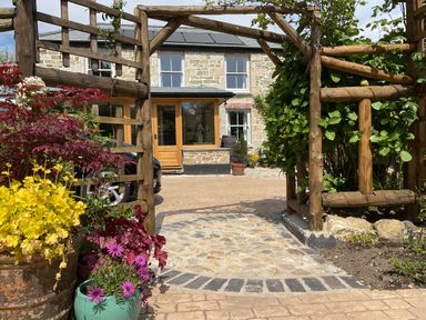A stone house with wooden doors viewed through a wooden garden arch with potted plants at Woodbine Cottage in Mylor Bridge Nr Falmouth