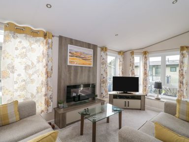 A living room with sofas glass coffee table television and floral curtains at Gwydn Lodge in Downton Hampshire