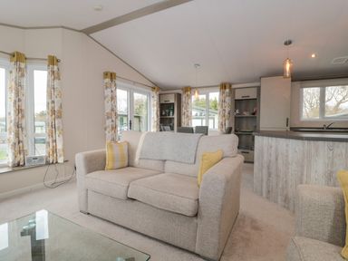 A living room with a beige sofa yellow cushions and floral curtains at Gwydn Lodge in Downton Hampshire