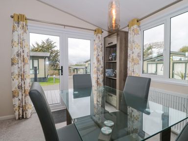 A dining area with a glass table and four chairs near windows and floral curtains at Gwydn Lodge in Downton Hampshire