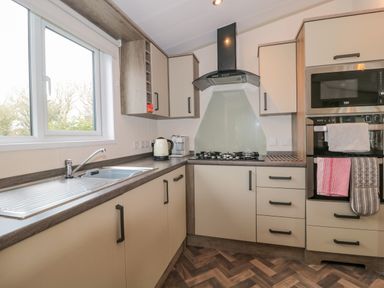A kitchen with a window above a sink a kettle coffee machine a gas stove with extractor and built in microwave and oven at Gwydn Lodge in Downton Hampshire