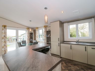 A kitchen with a wooden countertop dining table chairs windows and floral curtains at Gwydn Lodge in Downton Hampshire