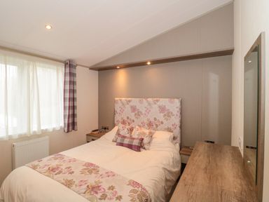 A bedroom with a double bed floral headboard two side tables a window with curtains and a wooden dresser with mirror at Gwydn Lodge in Downton Hampshire