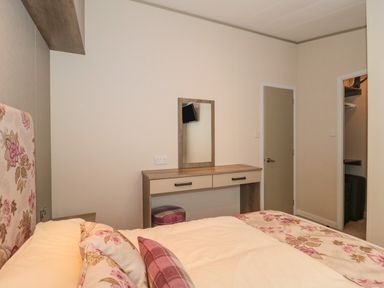 A bedroom with a floral bedspread a dressing table with a mirror and two doors at Gwydn Lodge in Downton Hampshire