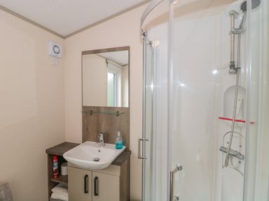 A bathroom with a sink cabinet mirror hand soap and a curved glass door shower at Gwydn Lodge in Downton Hampshire