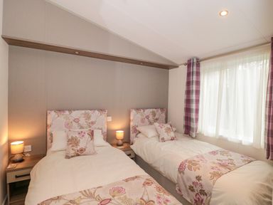 A bedroom with two single beds with floral bedding and matching pillows beside a window with plaid curtains at Gwydn Lodge in Downton Hampshire