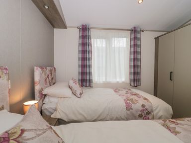 A bedroom with two single beds white bedding floral cushions and plaid curtains at Gwydn Lodge in Downton Hampshire