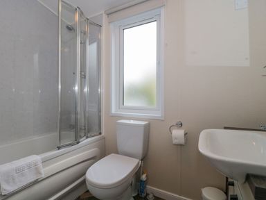 A bathroom with a bathtub and shower, a toilet, and a sink at Gwydn Lodge in Downton Hampshire