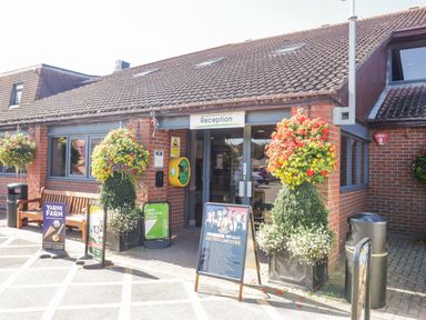 The entrance to a brick building with a reception sign hanging above the door and potted plants with flowers on either side at Gwydn Lodge in Downton Hampshire
