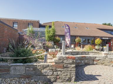 An outdoor area with stone walls plants and a building with a reception sign at Gwydn Lodge in Downton Hampshire