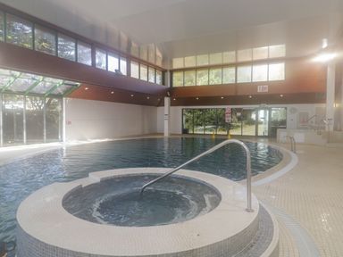 An indoor swimming pool with a round hot tub in the foreground and large windows at Gwydn Lodge in Downton Hampshire