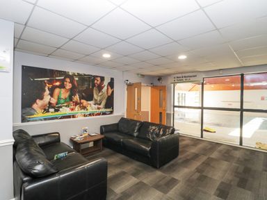 A lounge area with two black leather sofas a coffee table and a large window overlooking an indoor pool area at Gwydn Lodge in Downton Hampshire