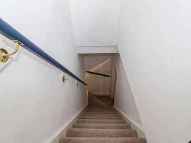 A carpeted staircase with white walls and a blue handrail at Snowflake Cottage in Windermere
