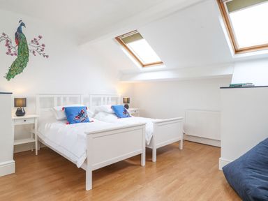 A bedroom with two white beds and blue pillows under skylight windows at Snowflake Cottage in Windermere
