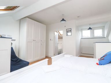 A bedroom with white wardrobes a blue chair a skylight and a bed with white bedding and a blue cushion at Snowflake Cottage in Windermere