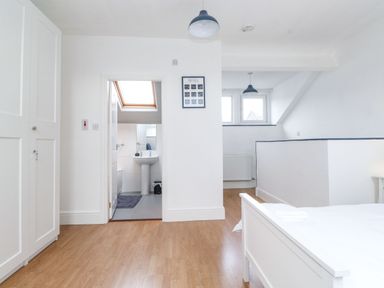 A bedroom with a white bed white wardrobe wooden floor and an adjoining bathroom at Snowflake Cottage in Windermere