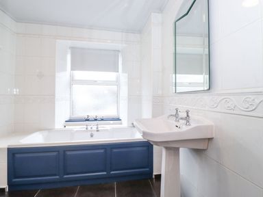 A bathroom with a bathtub with blue panel and a sink with a mirror above at Snowflake Cottage in Windermere