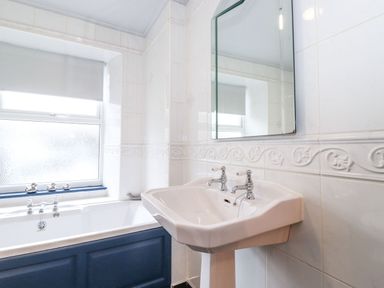 A bathroom with a white pedestal sink and a bathtub with blue paneling at Snowflake Cottage in Windermere