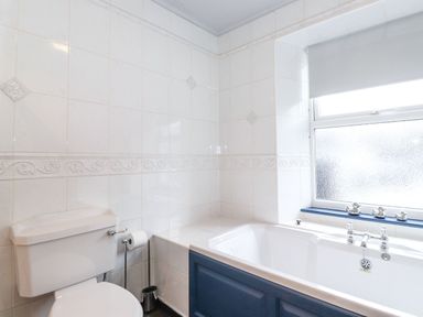 A bathroom with a white toilet beside a bathtub under a window with three small duck ornaments on the windowsill