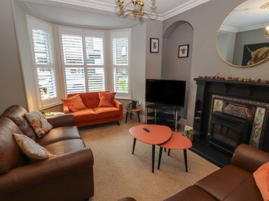 A living room with brown and orange sofas a black fireplace and a television at Snowflake Cottage in Windermere