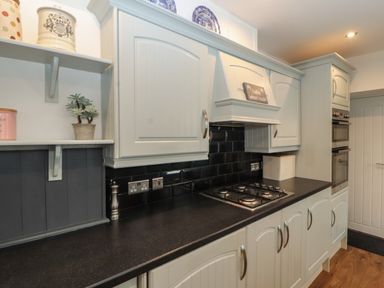 A kitchen countertop with gas stove and white cabinets with black tiled backsplash at Snowflake Cottage in Windermere