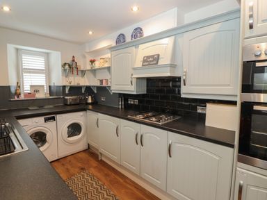 A kitchen with white cabinets black countertops a washing machine dryer and a gas stove at Snowflake Cottage in Windermere