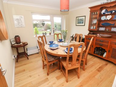 A dining room with a round wooden table set for six and a wooden cabinet displaying dishes at Glynderi in Cilgerran