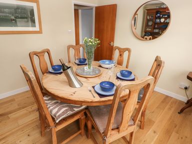 A dining room with a round wooden table set with blue bowls plates wine glasses and a vase of flowers at Glynderi in Cilgerran