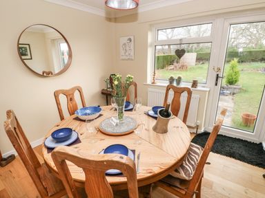 A dining room with a round wooden table set for four with blue bowls and plates a vase with flowers and a wine bottle in a cooler at Glynderi in Cilgerran