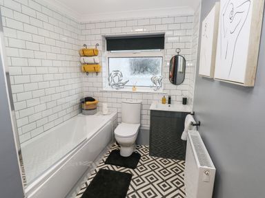 A bathroom with a bathtub toilet sink mirror and wall art at Glynderi in Cilgerran