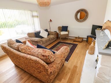 A living room with two sofas a wicker chair a rug and a TV on a stand at Glynderi in Cilgerran