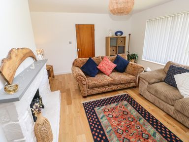 A living room with two sofas a patterned rug a white fireplace and a wooden shelf at Glynderi in Cilgerran