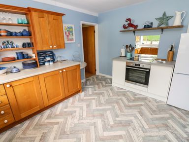 A kitchen with wooden cabinets blue wall decorations and a white oven at Glynderi in Cilgerran