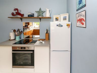 A kitchen corner with a white oven and countertop next to a white refrigerator with wall art and a shelf with decorations at Glynderi in Cilgerran