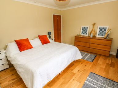 A bedroom with a large bed with white bedding and red pillows a wooden dresser with decorative items and framed pictures at Glynderi in Cilgerran